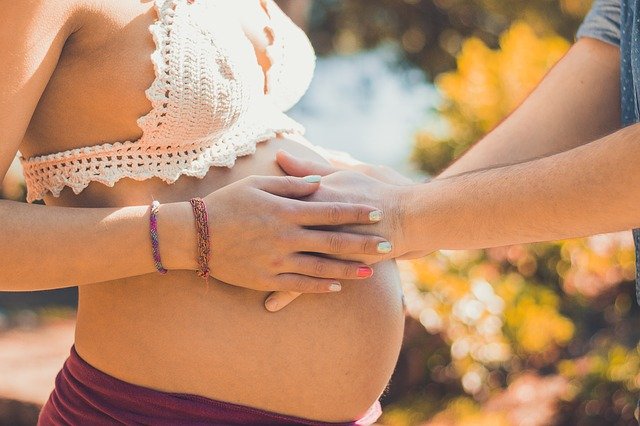 Pregnant woman with partner's hands on stomach